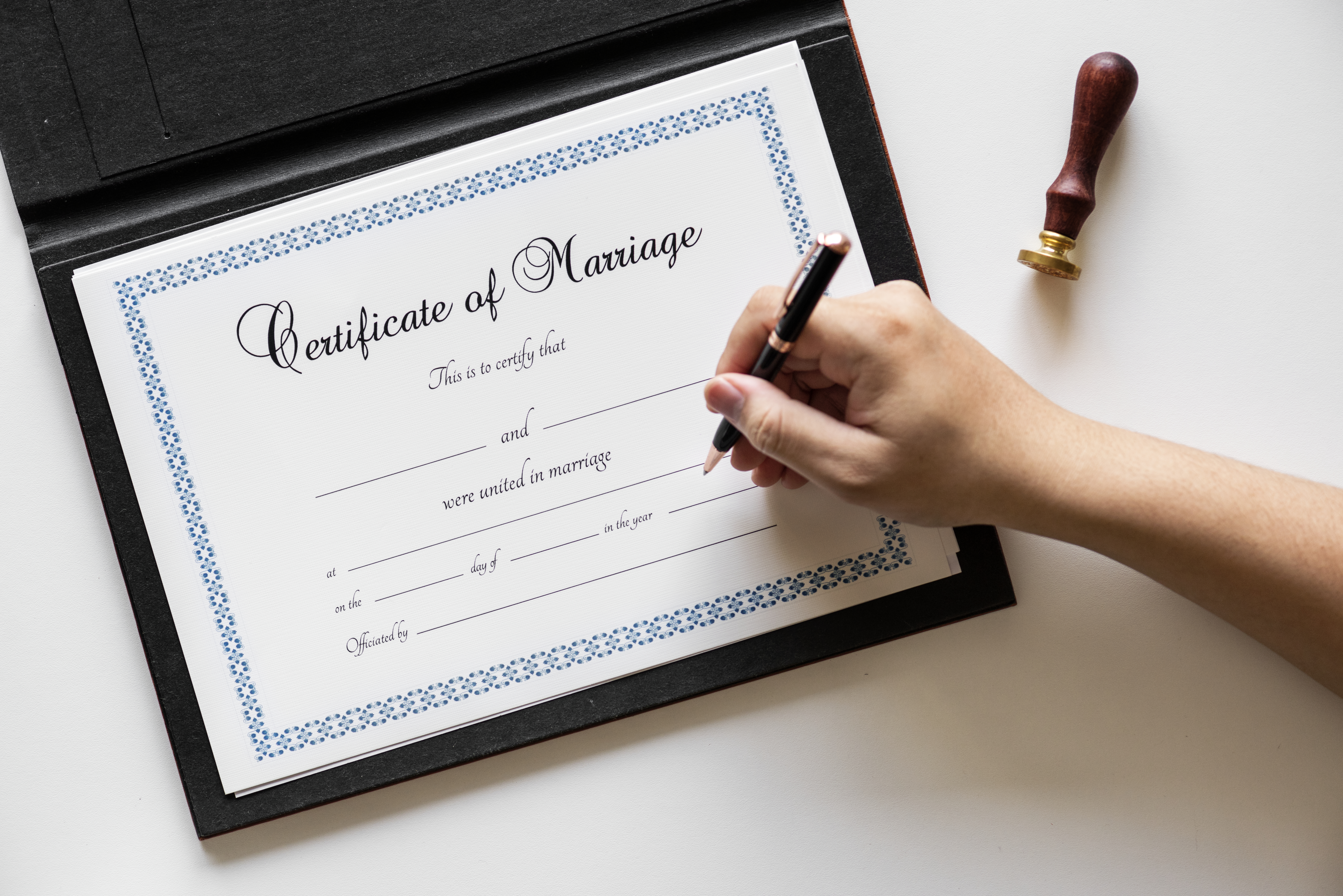 White hand holding pen gets ready to sign a certificate of marriage 