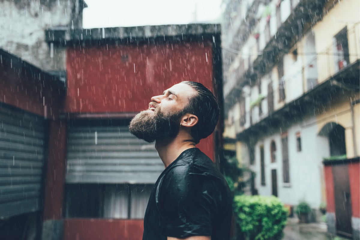 30-something bearded white male looking up at the rain with his eyes closed