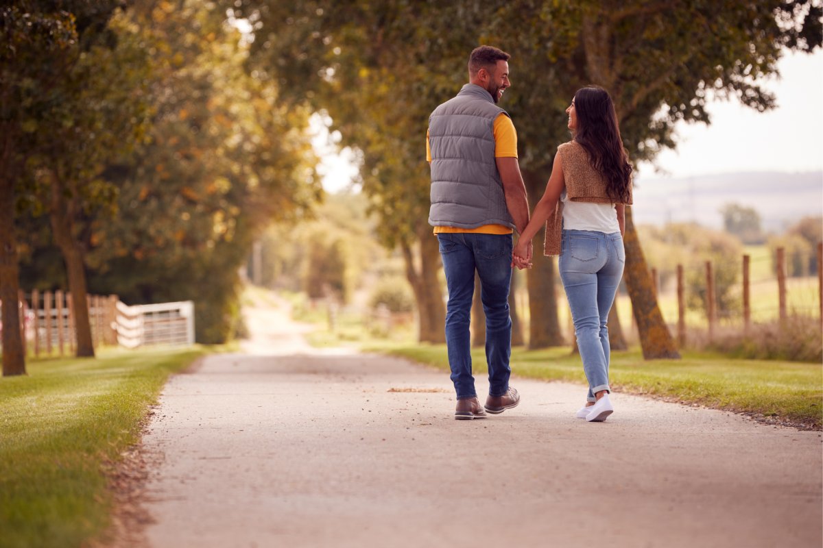 white 30-something couple walking down road holding hands looking at each other