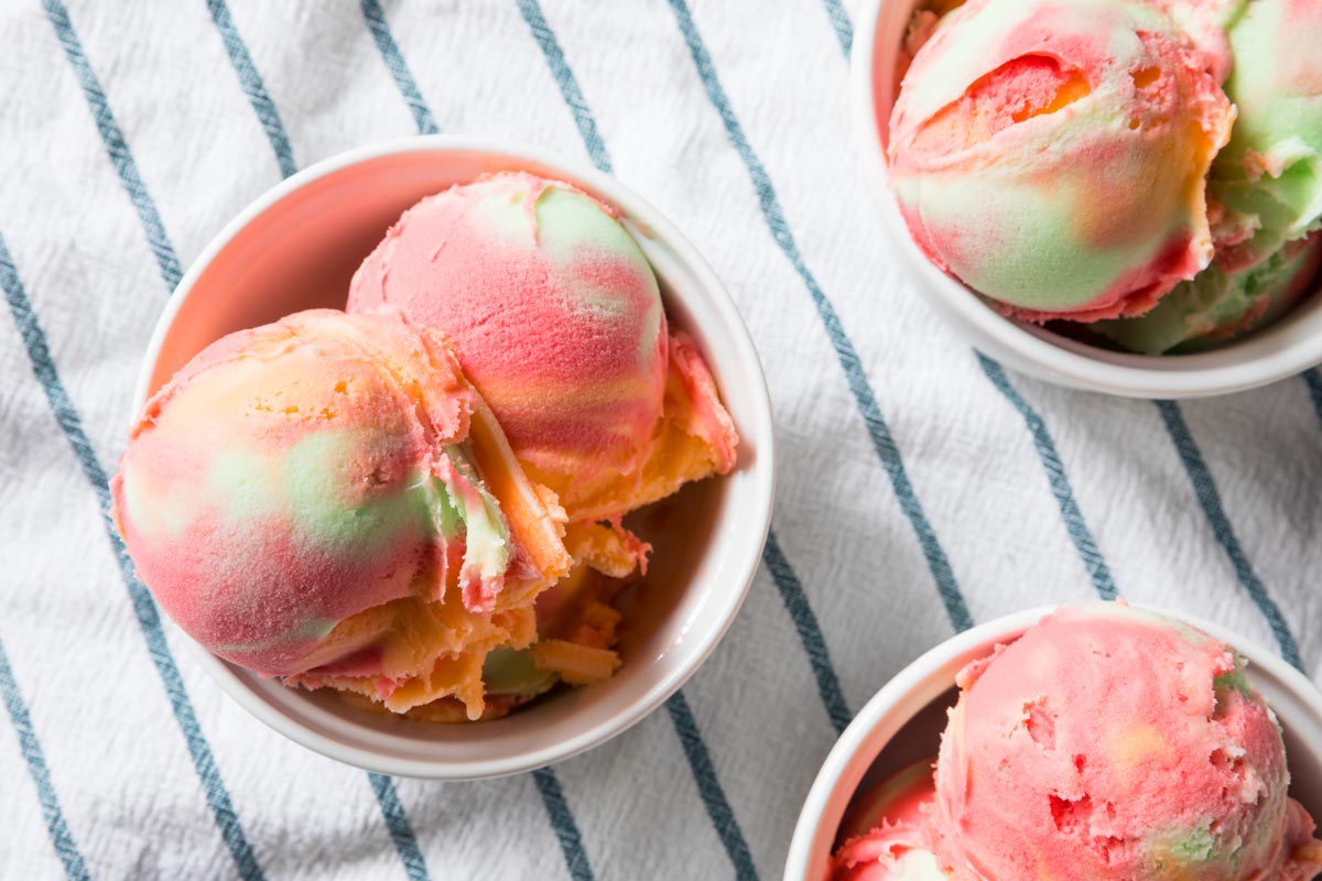 Colorful scoops of rainbow sorbet in white bowls on a striped white a blue tablecloth ideal as a refreshing dessert option for warm-weather events