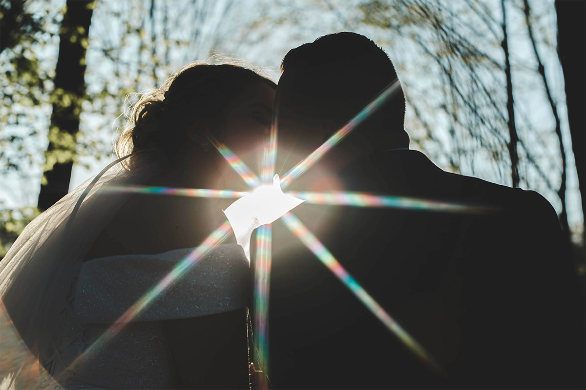 couple in the woods leaning together with a sun beam coming through at their shoulders