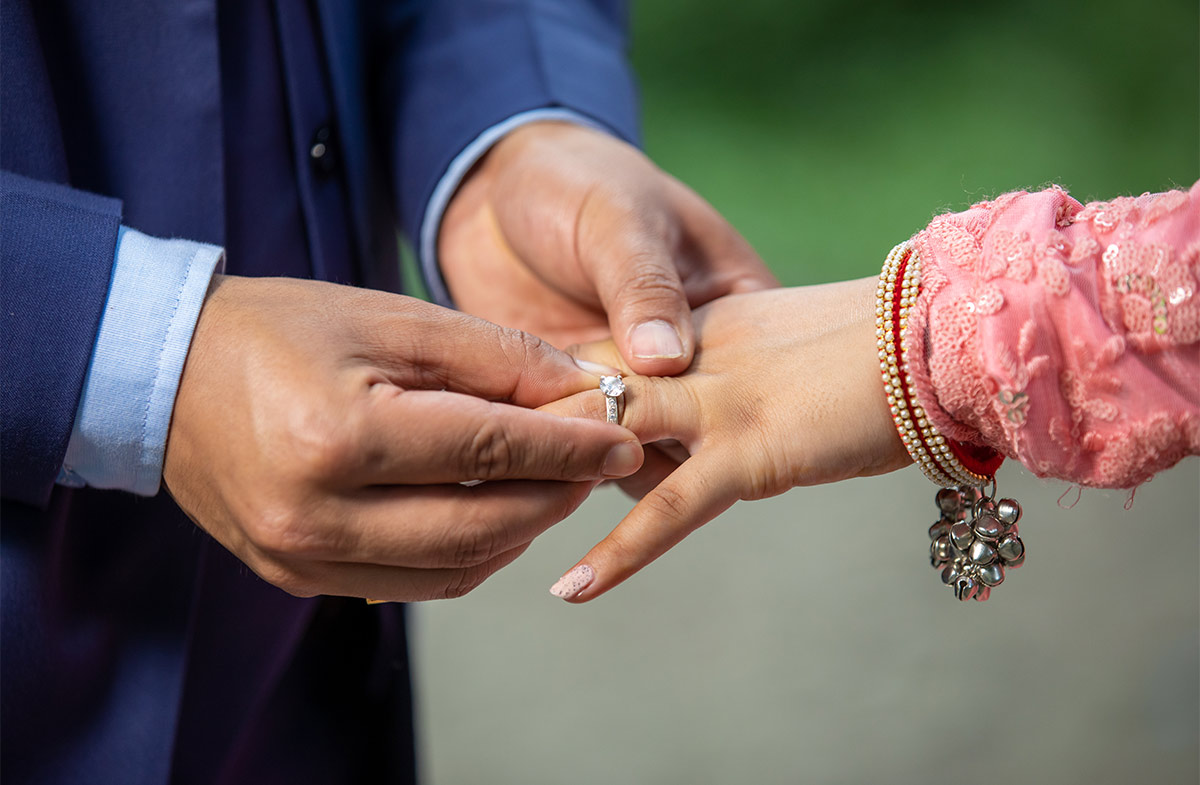 A woman’s hand wearing a bracelet with bells and a man is placing a wedding ring on her finger