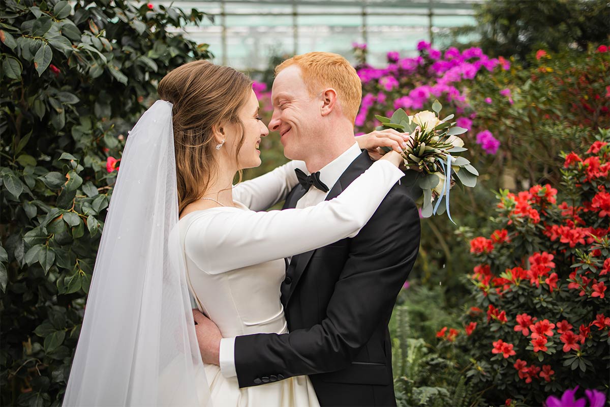 20 Somethings white man in suite and women in wedding dress, hugging each other and leaning in for a kiss in a botanical garden