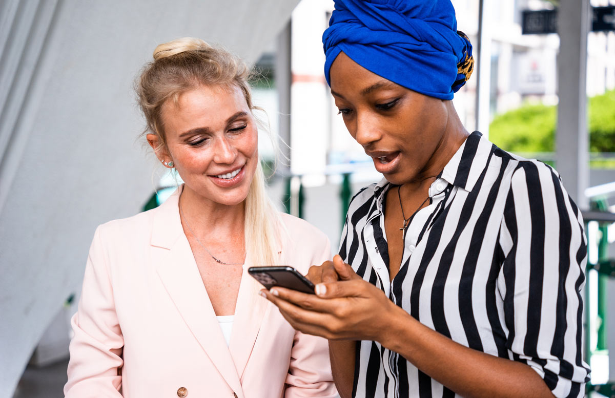 Black 30-year-old woman showing a white 30-year-old bridal consultant a wedding dress on her phone. 