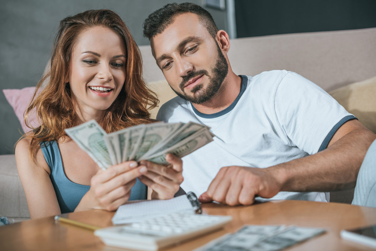 White couple in their early 30s counting fanned out dollar bills 