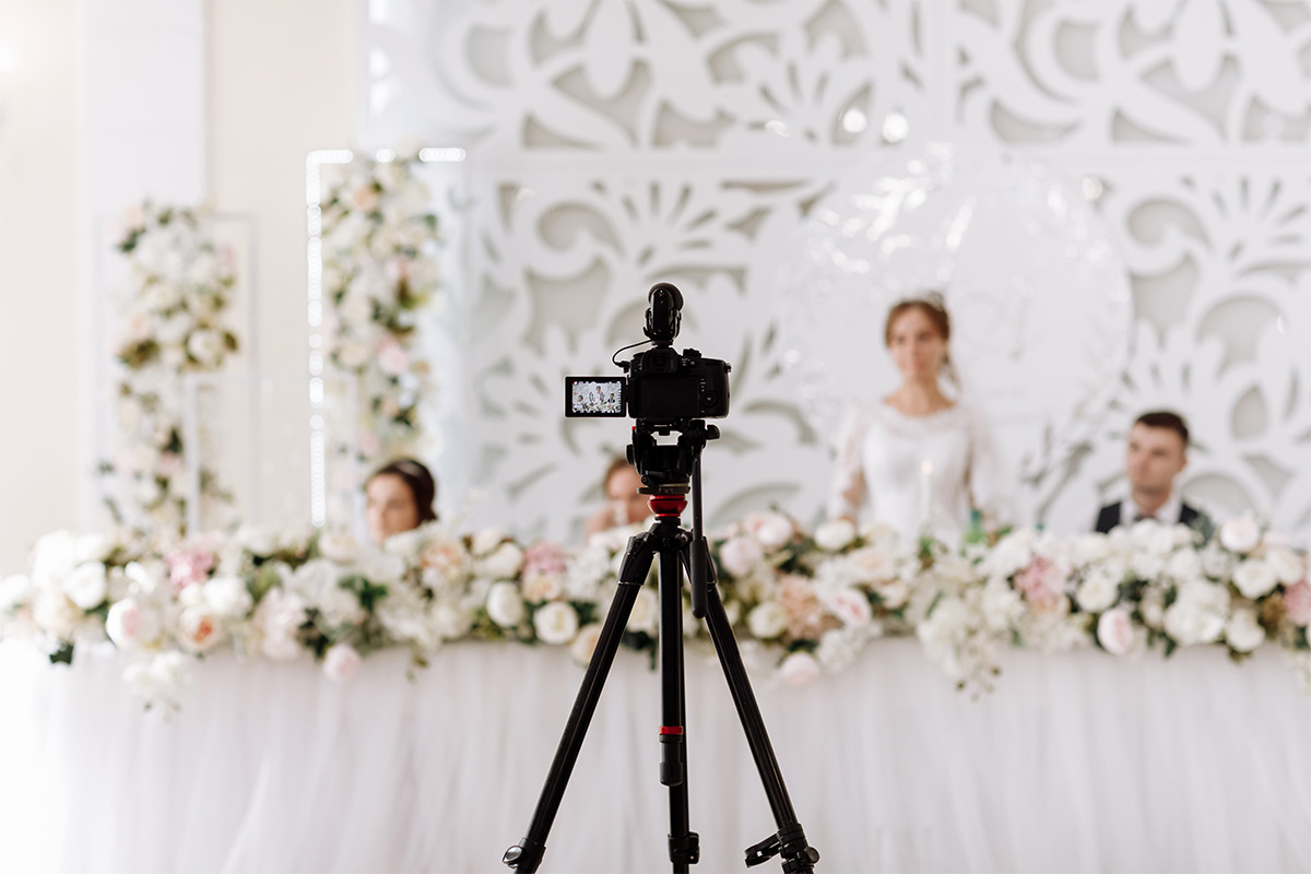 Camera set up to take photos in front of a bride and groom with two bridesmaids at a table with large white flowers.