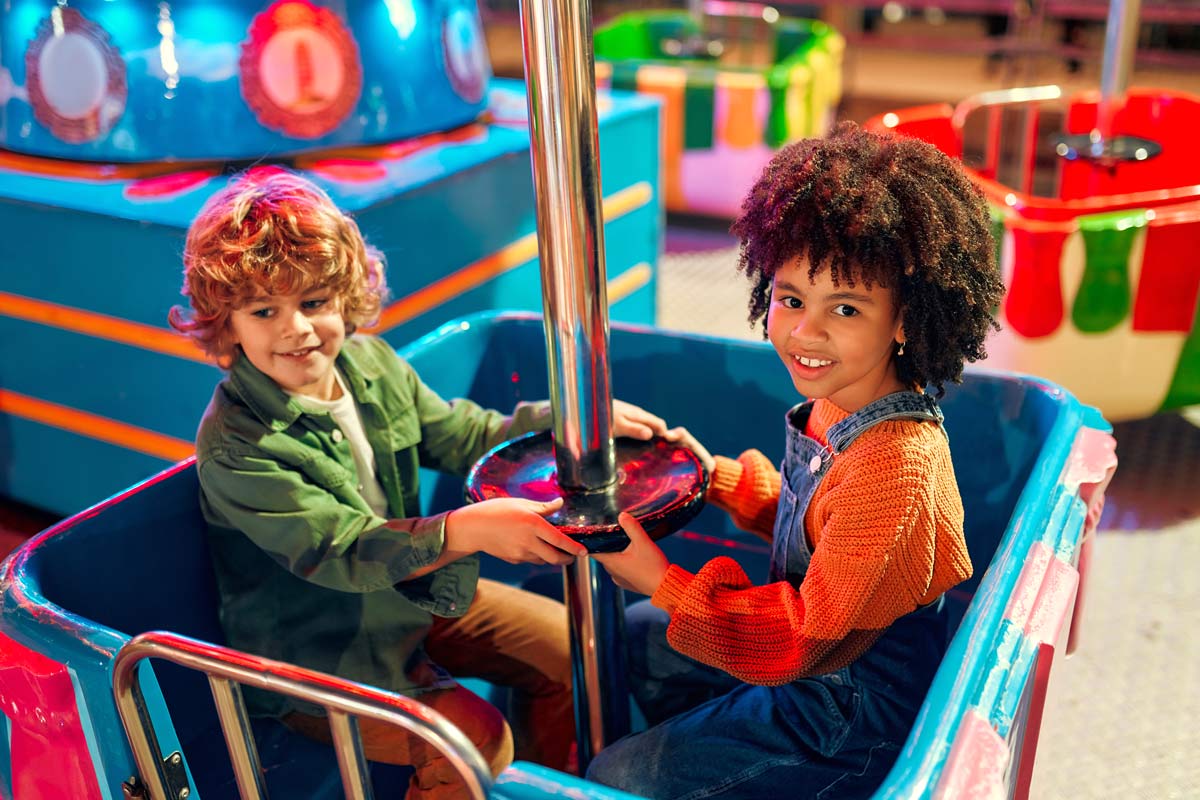 Two multi-racial children age 8-10 ride a spinning ride and smile at an amusement park