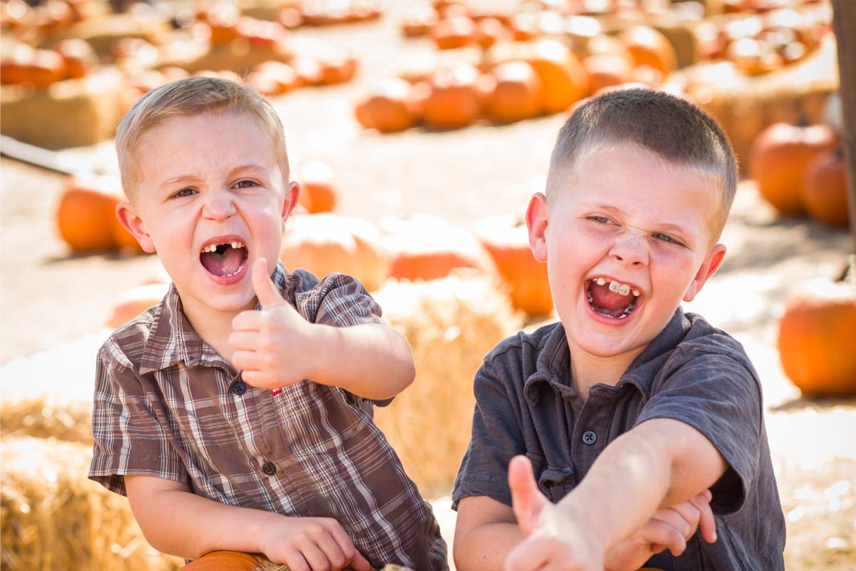 Two young white boys age 8-10 giving a thumbs up with excited faces while getting pumpkins at a pumpkin patch