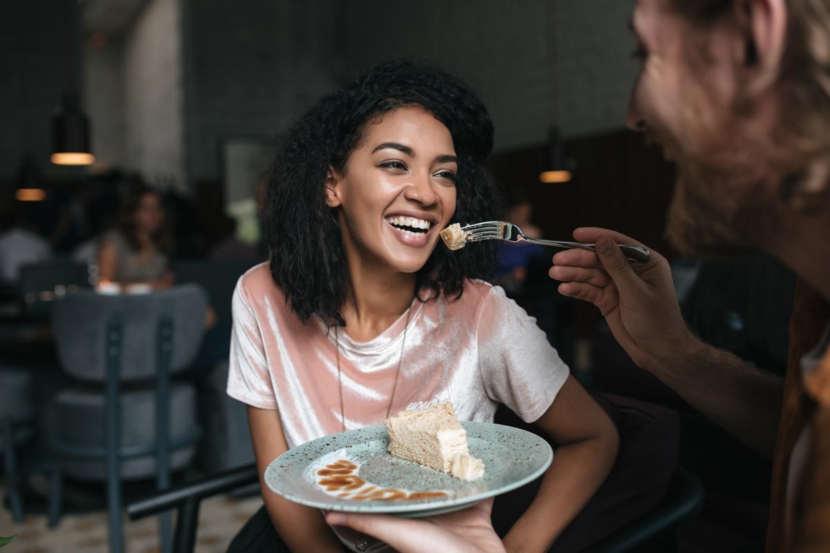  A 20 something black woman at a restaurant getting fed a piece of cake while laughing