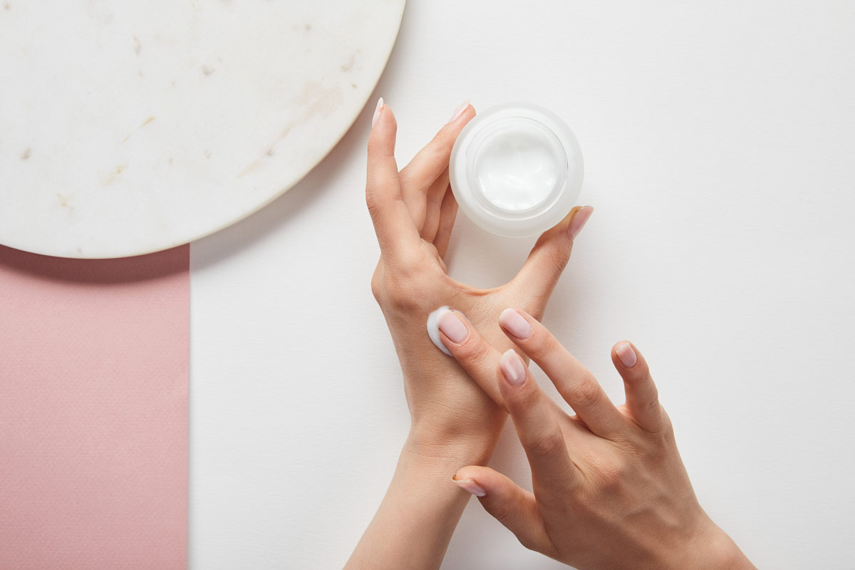 White woman applying lotion from a small jar onto her hands.