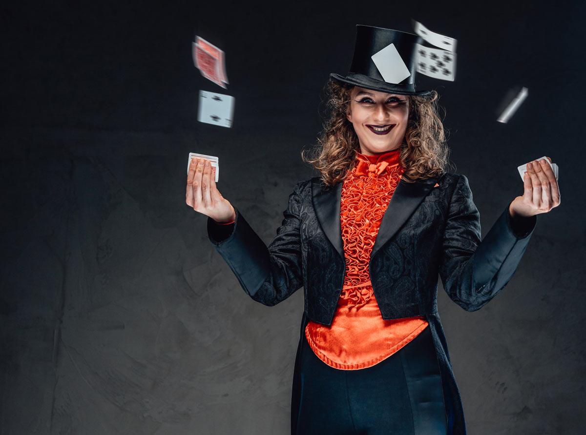 White female magician in her 40s  in black and red clothing shuffling playing cards.