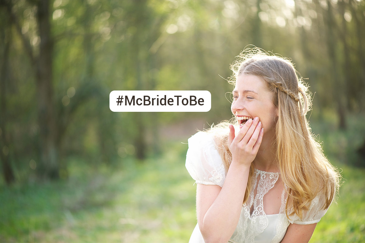 white 20 something woman wearing white top laughs into her hand while standing in a sunny forest