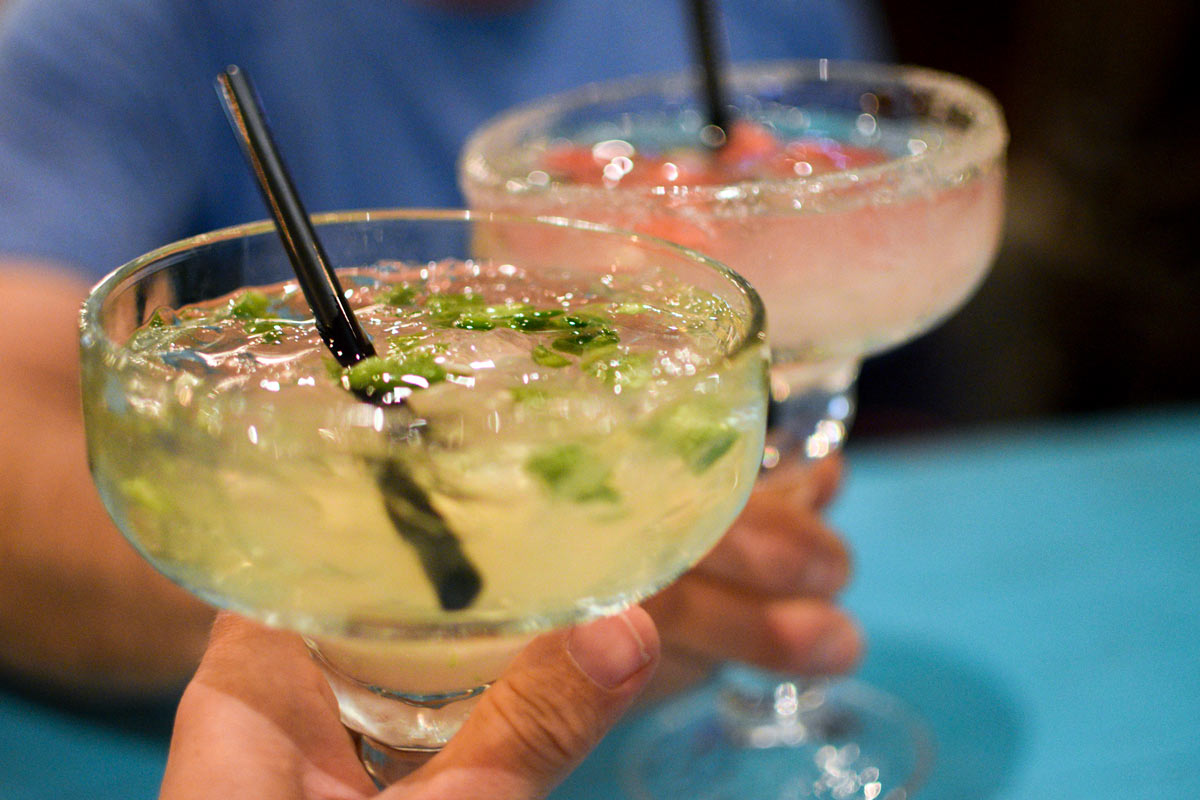 Two margarita classes with black straws clinking glasses