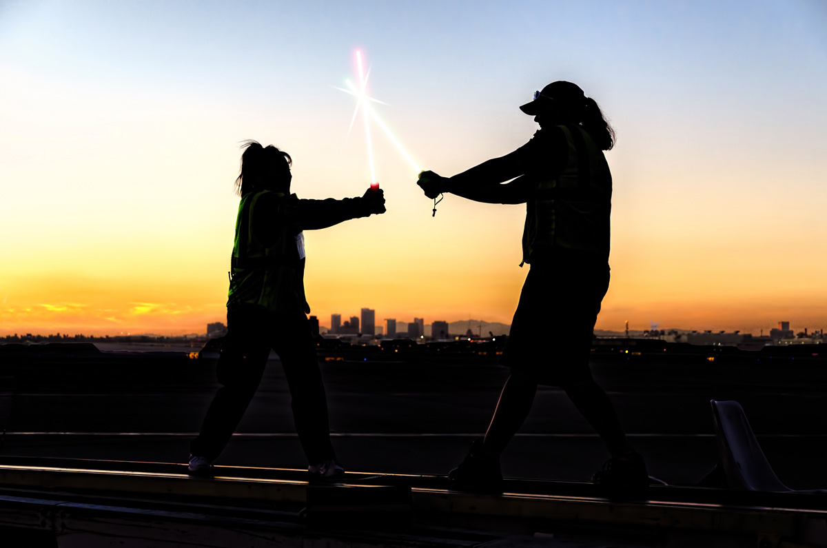  Outline of Man and women fighting with lightsabers on the horizon in the city during sunset. 