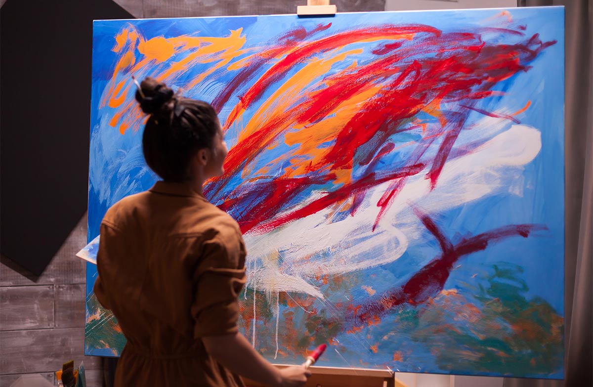 Young white woman stands and paints a large abstract art piece in an indoor studio