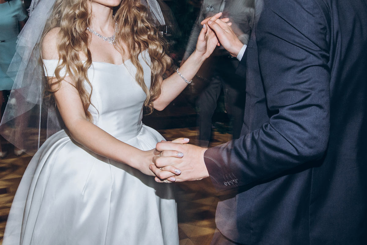 blonde bride wearing veil while dancing with well-dressed man on the dance floor