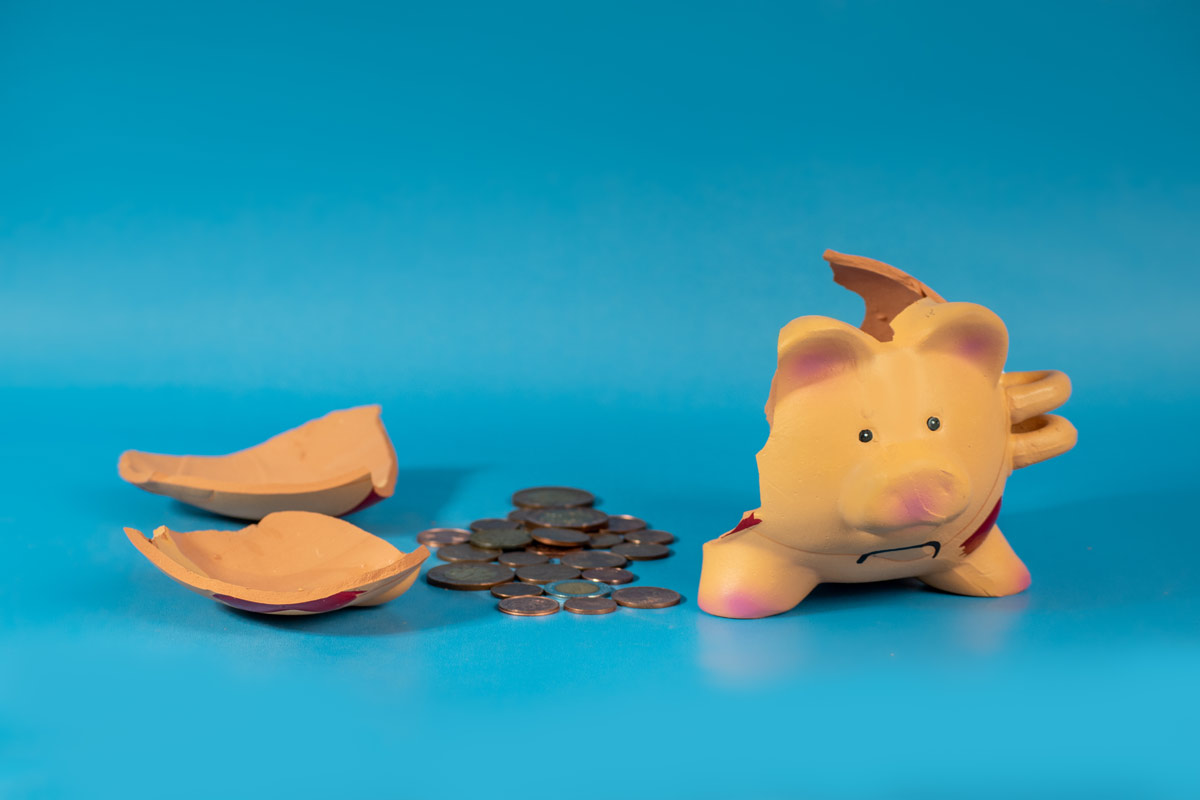 Frowning piggy bank was smashed open leaving coins on a blue background.