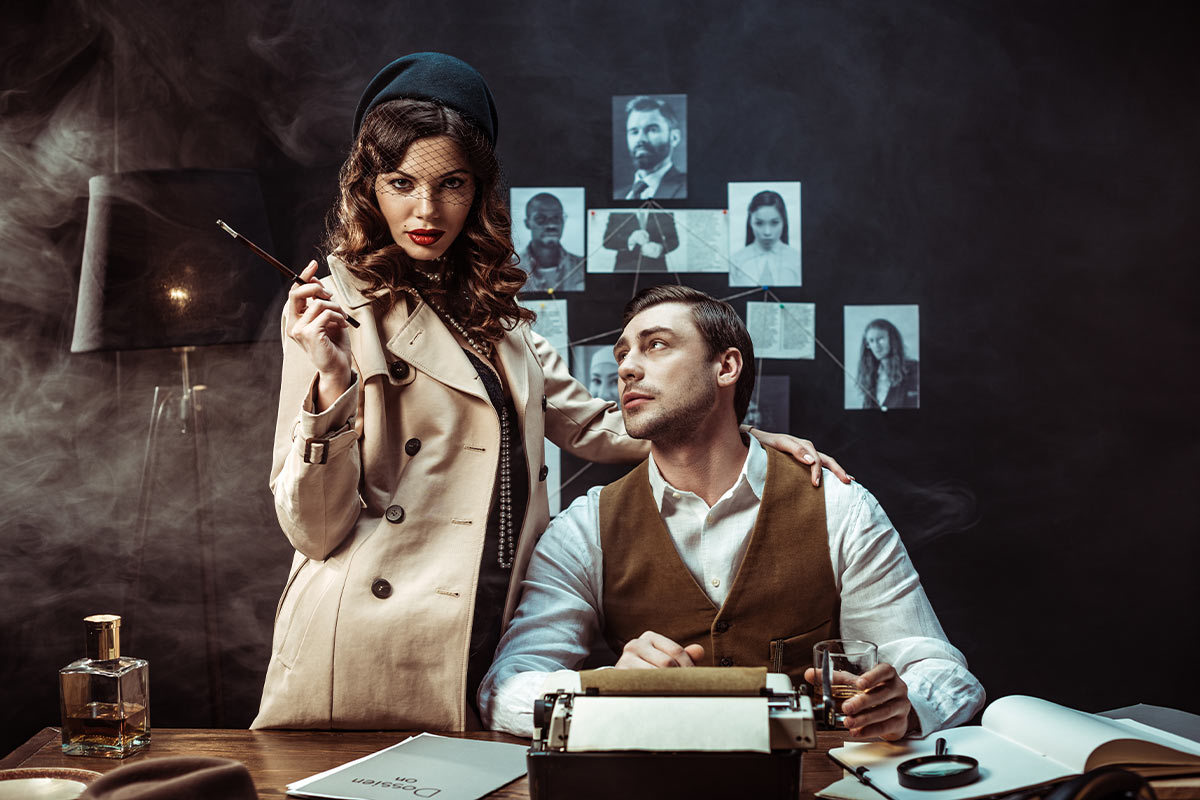 white man in a detective outfit with a glass in his hand sitting at a table with a typewriter and looks up at a woman in a detective outfit that has her left hand on his shoulder and a wooden device in her right hand in the background there are pictures of suspects in black and white that are connected by string