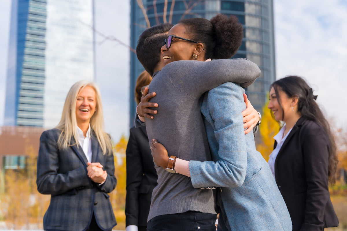 A middle aged black man and woman hugging with smiling people standing behind them