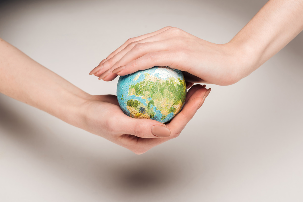 Womens hands holding a small planet earth with gray background. 