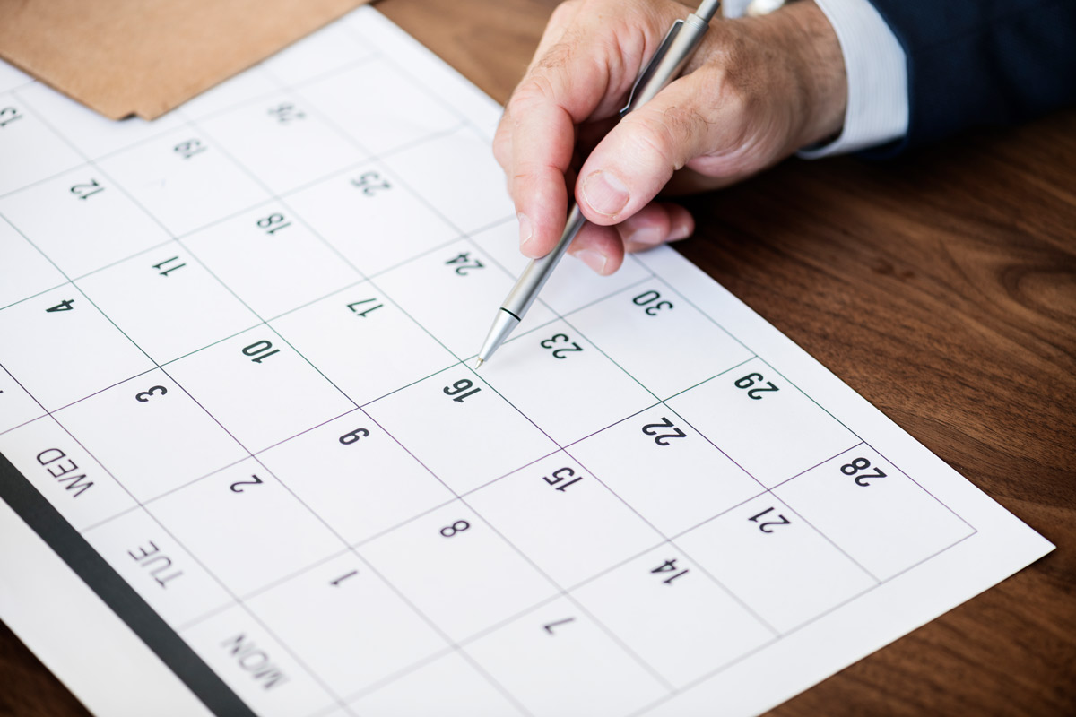 White 30-year-old man wearing a suit looking at his calendar to find the best date to schedule his friend’s bachelor party. 