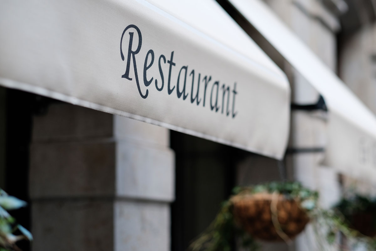 The outside of a restaurant with a white sign with black lettering saying “Restaurant”.