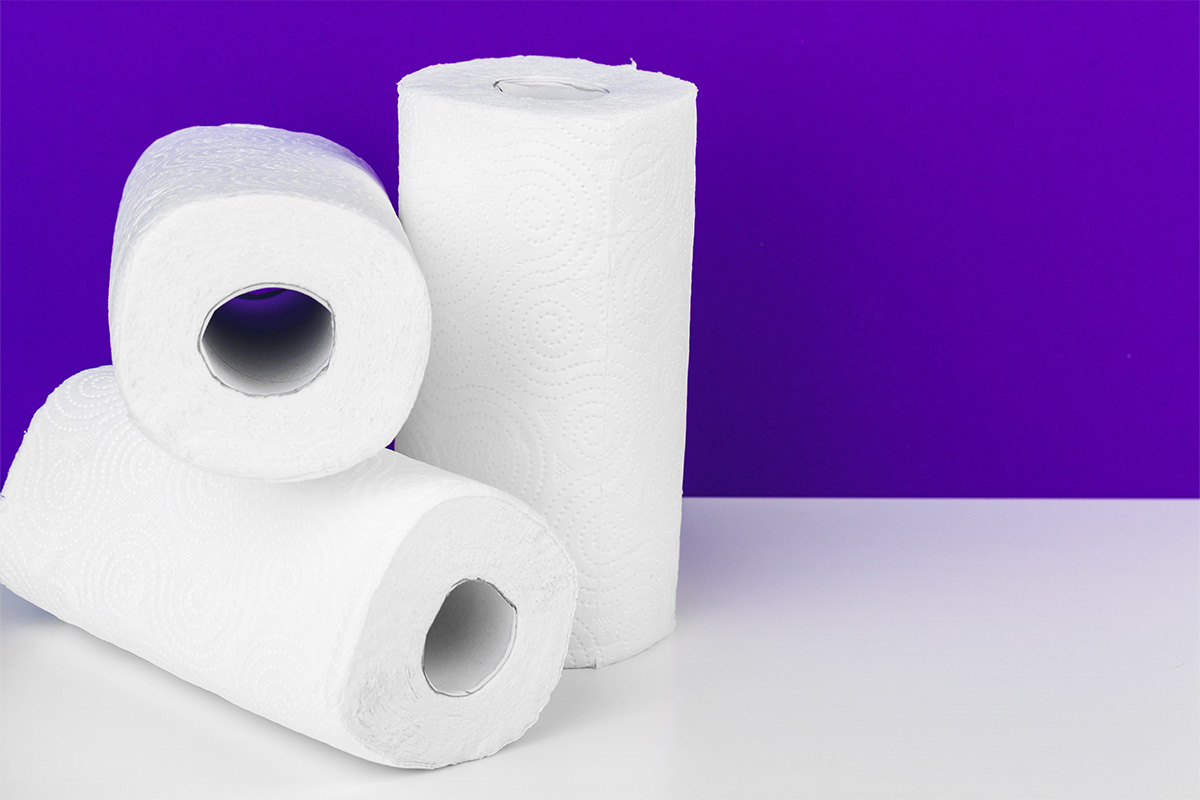 three rolls of paper towels, two stacked horizontally and one vertically, in front of a purple background