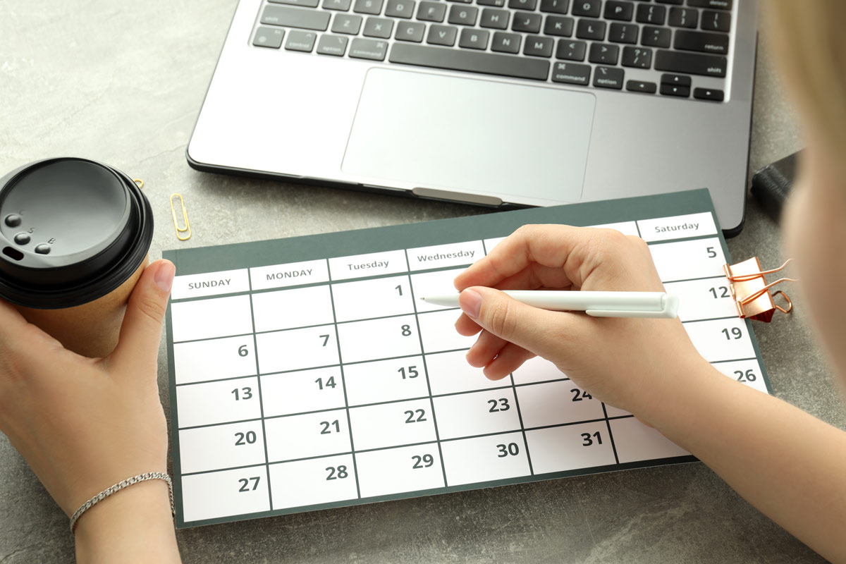 White 25-year-old woman checking her calendar to book a party bus for her and her friends, holding a coffee cup.