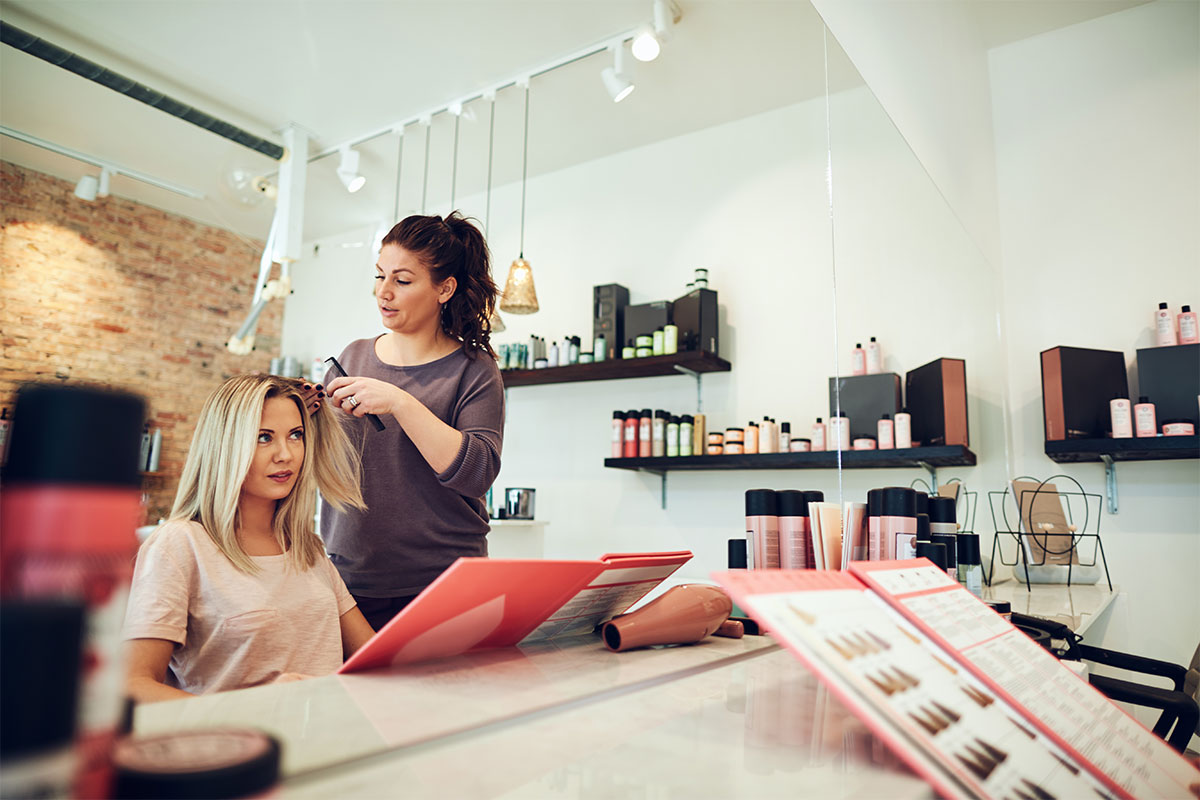 Woman getting hair styled in a salon while paying attention to the stylist in the mirror