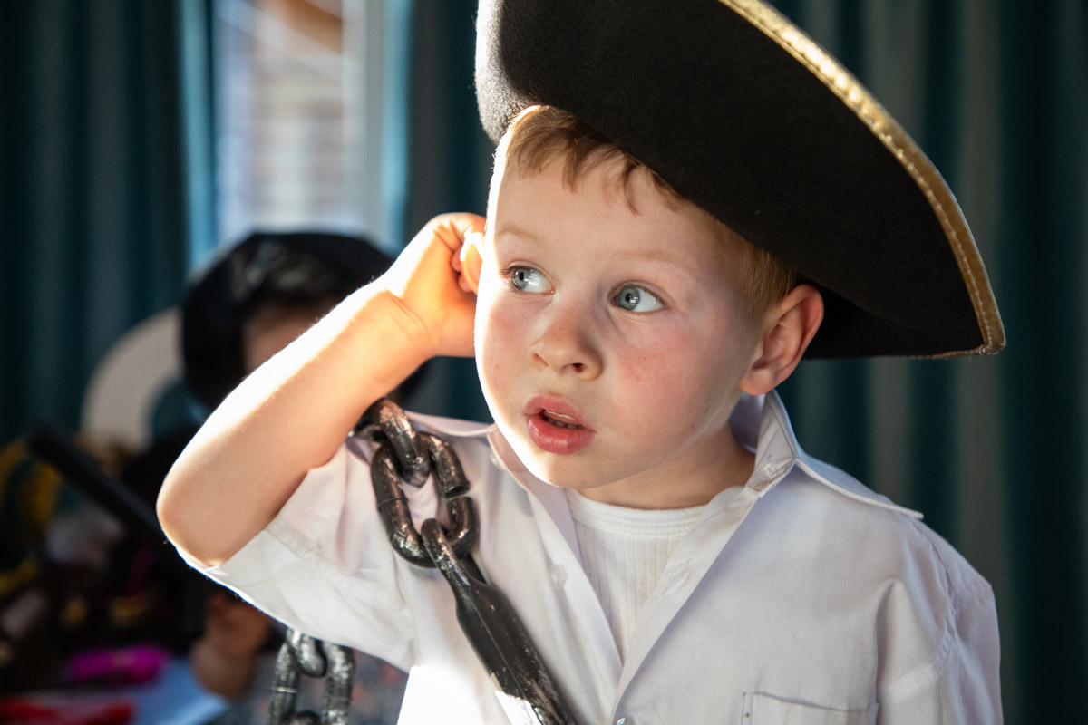 White little boy wearing a pirate costume and grabbing his ear while he looks off into the distance