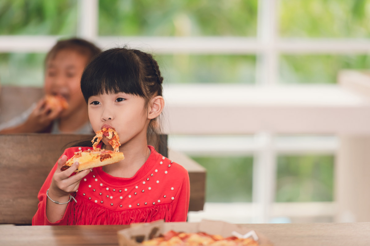 Asian little girl sitting on wooden bench eating a slice of pizza