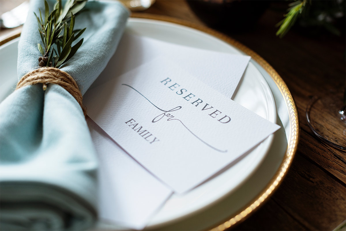 two white plates with a card that says “Reserved for Family” and a blue napkin with a plant on it sit on a wooden table