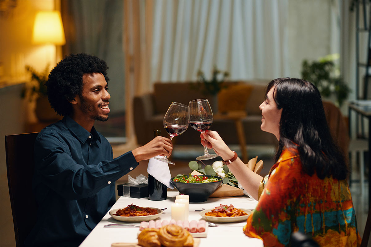 Young diverse couple toasting with wine glasses during a intimate dinner representing the importance of enjoying pre-wedding date nights