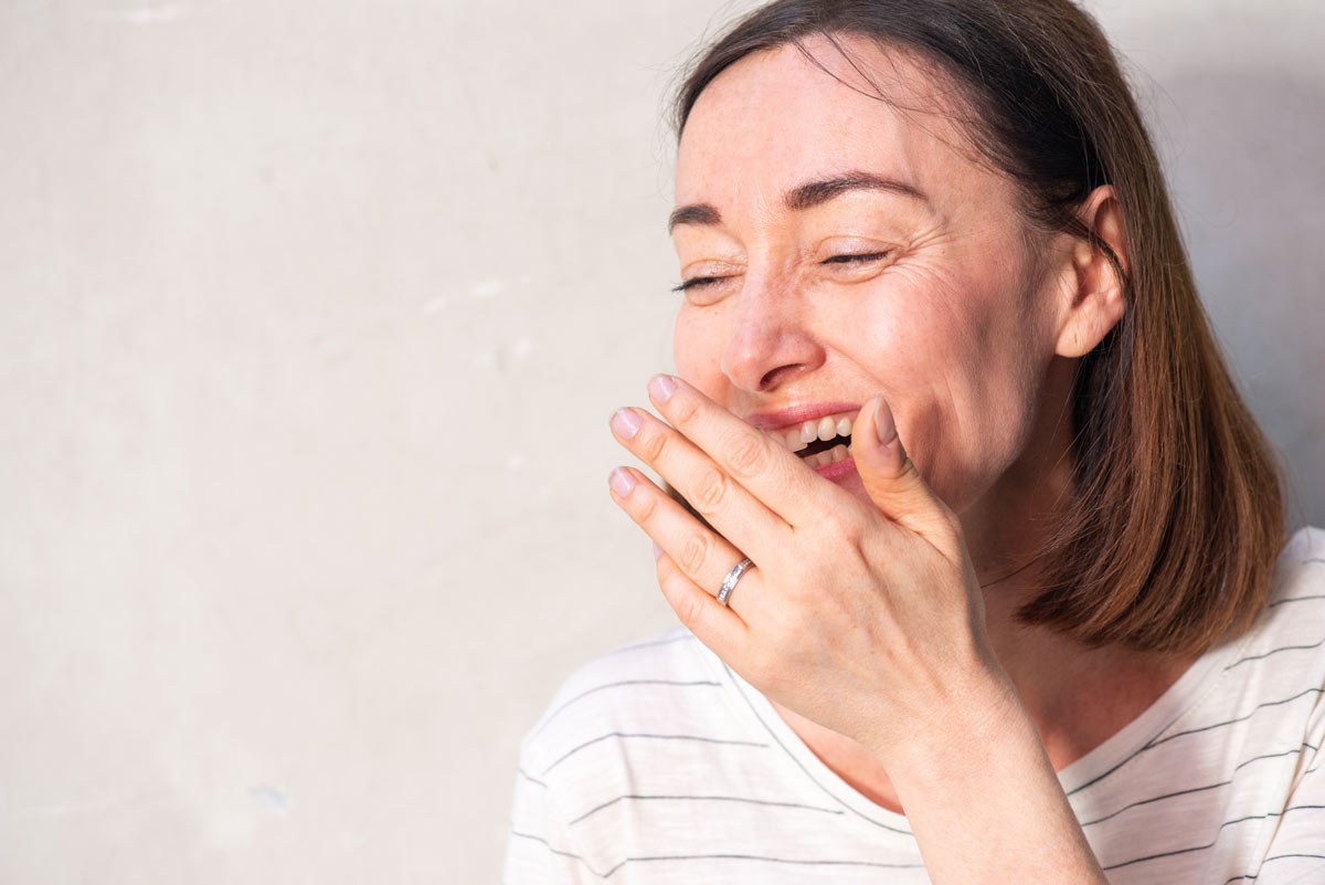 A laughing white 30-year-old woman covering her mouth with her hand.