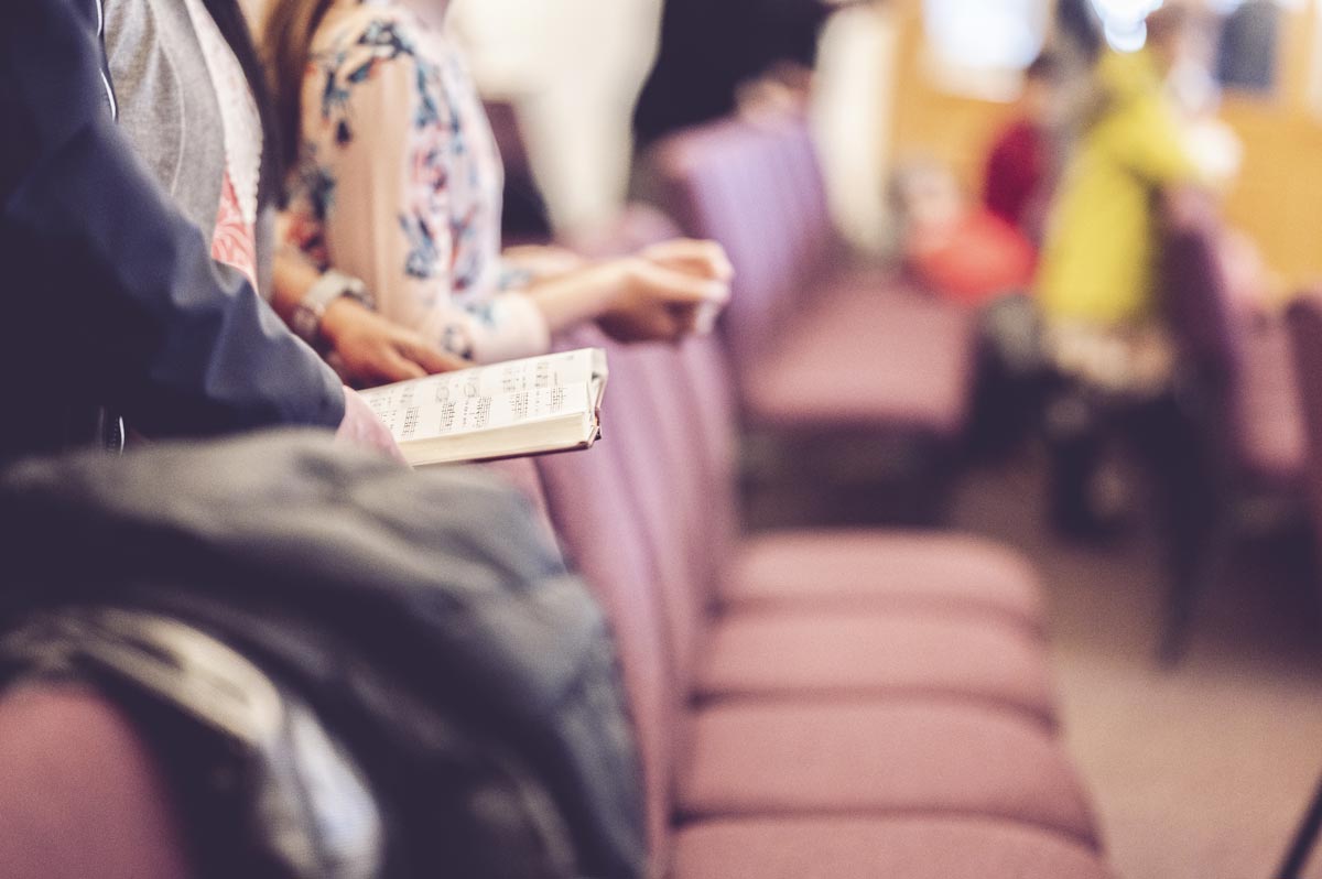 A man rests his songbook on a row of chairs in church.