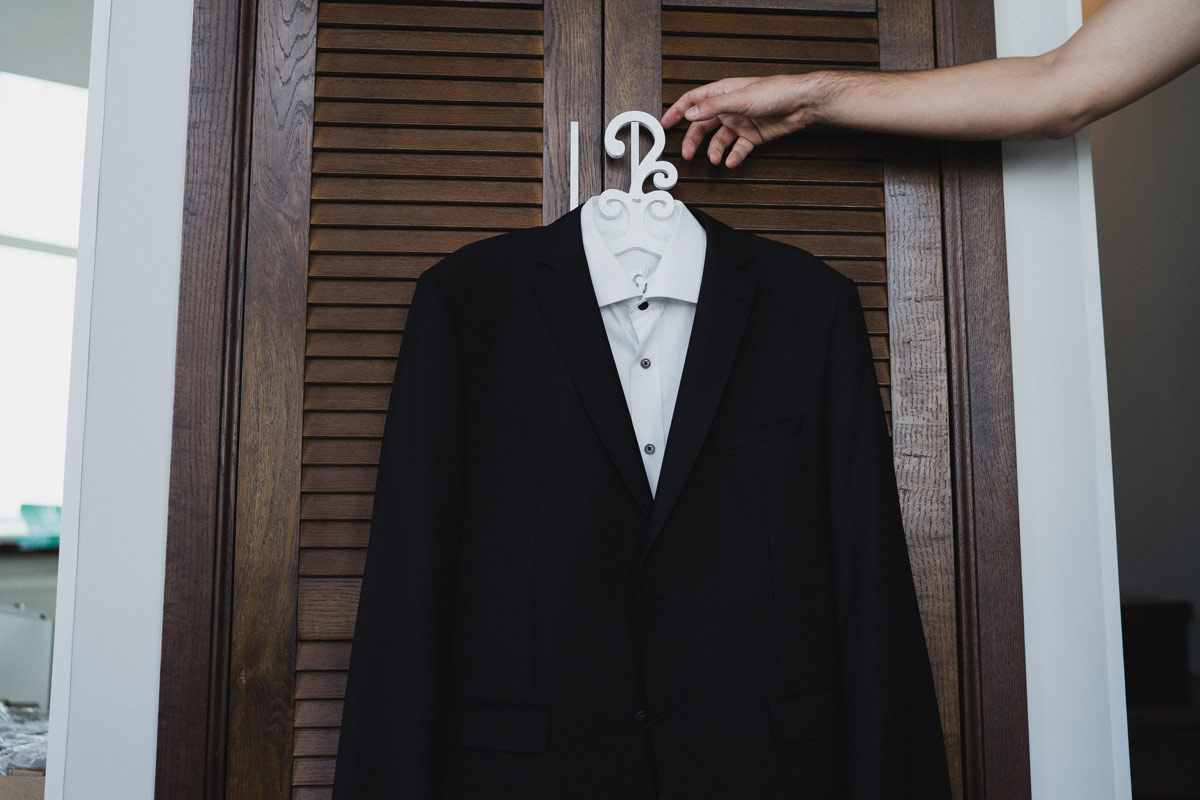 Black tuxedo with a white button up under it hung up on a closet door handle. 