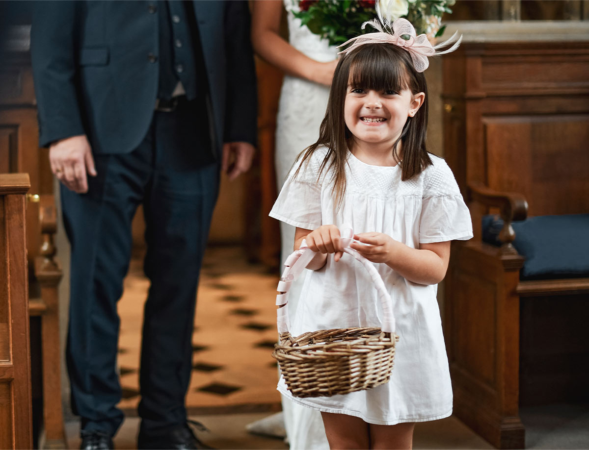 A white 10-year-old flower girl smiling and walking down the altar at a wedding as she holds a woven basket