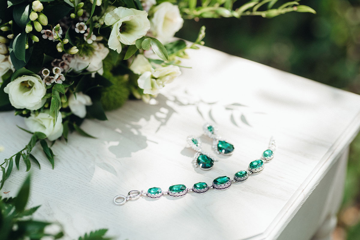 Emeralds jewelry piece laying on a table next to flowers 