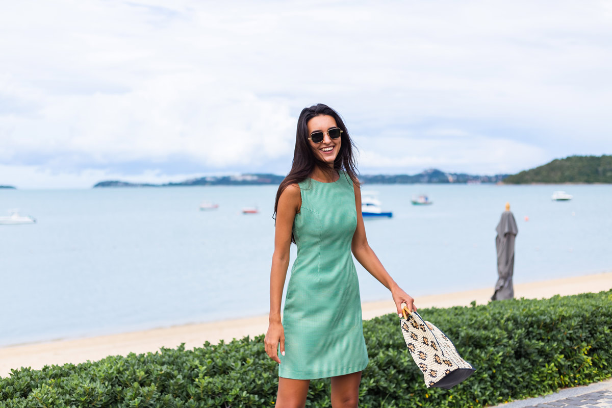 White 29-year-old brunette woman wearing a turquoise sheath dress by a beach. 