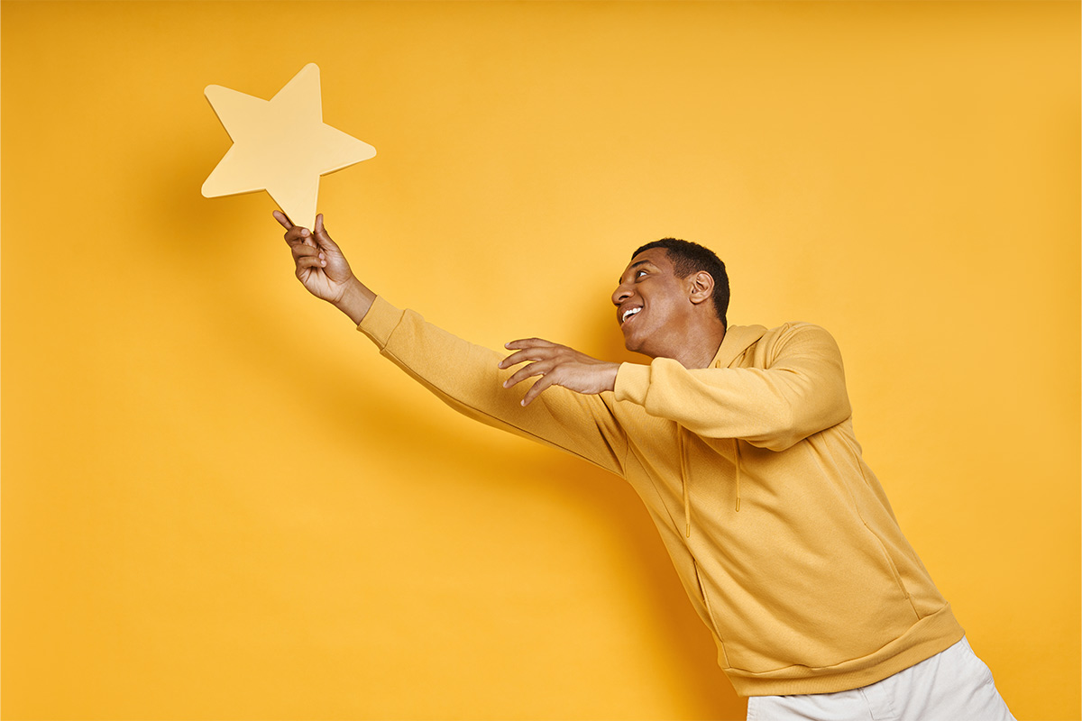 Black man in his twenties wearing yellow sweatshirt reaching for a yellow star prop with an all-yellow backdrop