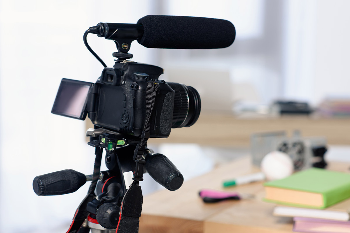 A camera is being set up to record a video in front of a table with books and supplies on it.