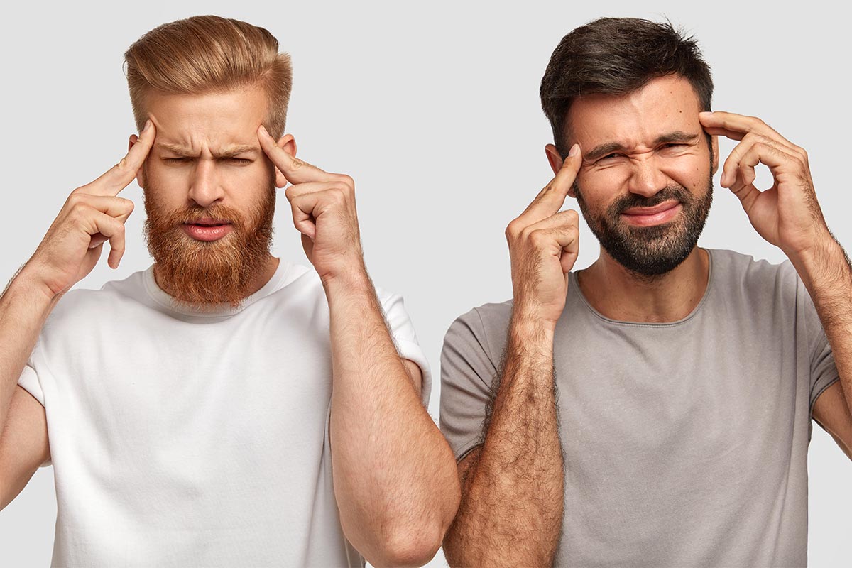  two bearded white men in their early 30s think really hard with their index fingers pressed against their temples while squinting