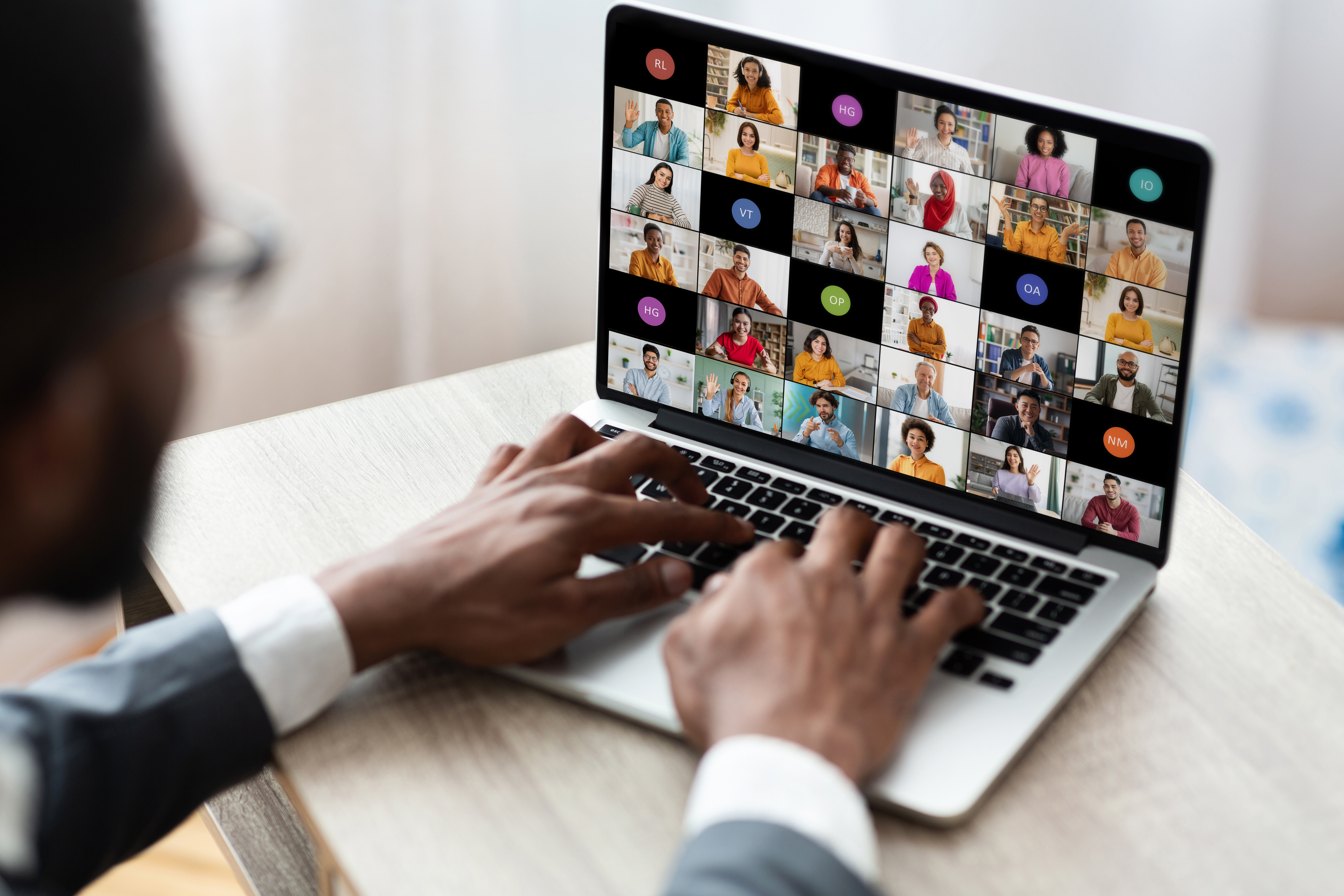 Black man types on laptop that shows a video call with many different people