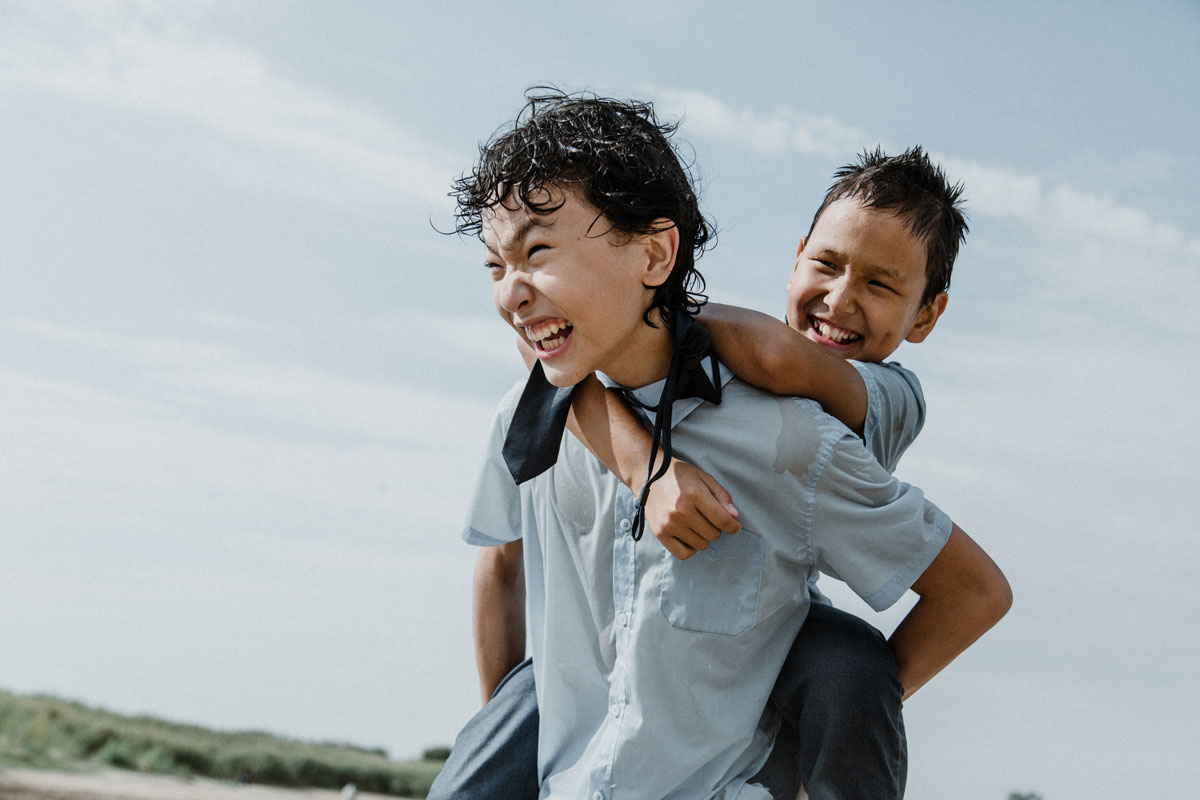 A laughing Asian older brother, age 10, takes his younger asian brother, age 5, on a piggy-back ride.