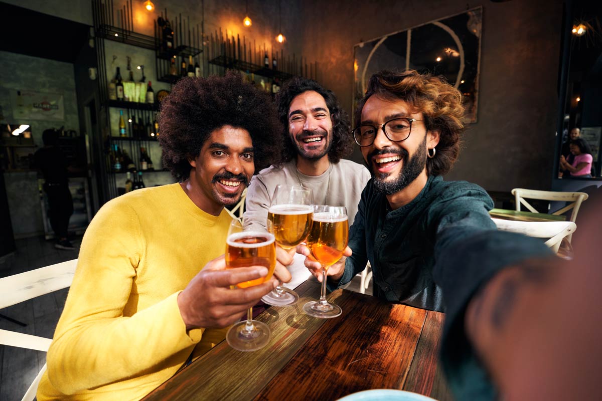 Three 30-year-old mixed-race friends sharing some beers while taking a selfie. 