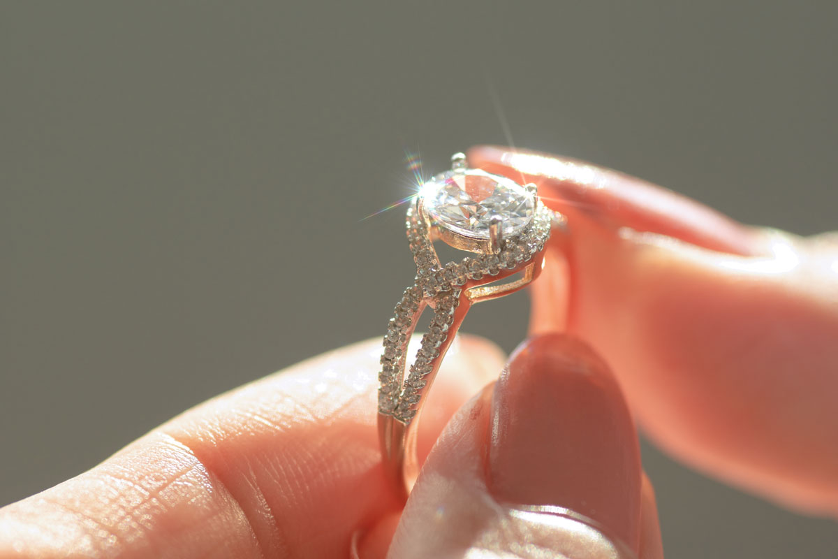 Hand holding diamond ring while it shines in the light with a sparkle