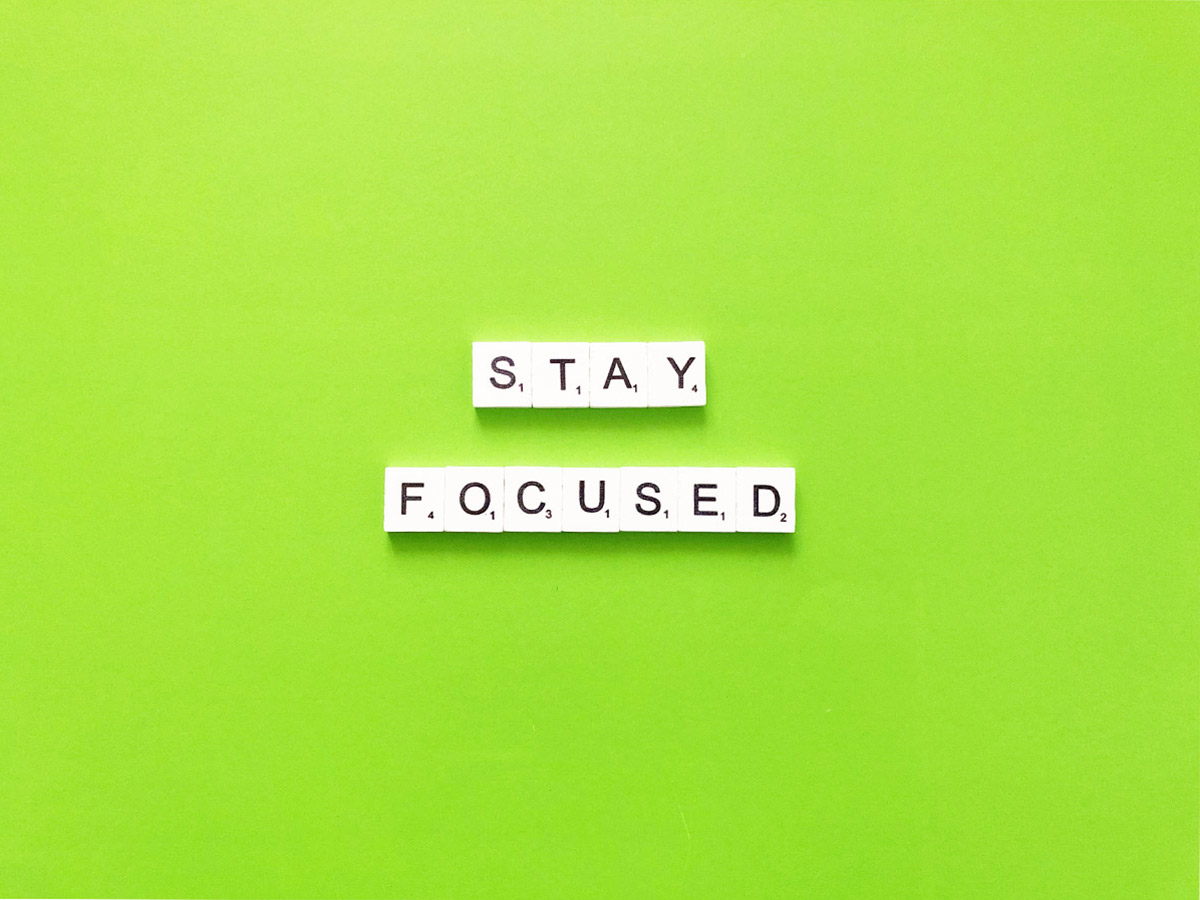 Scrabble letter pieces spelling out “stay focused” with a bright green background.