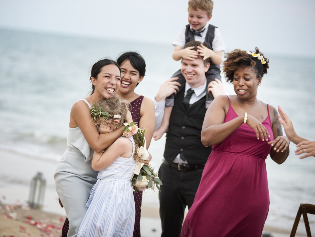 Group of mixed-race people smiling and having fun after wedding ceremony on the beach in front of the ocean.