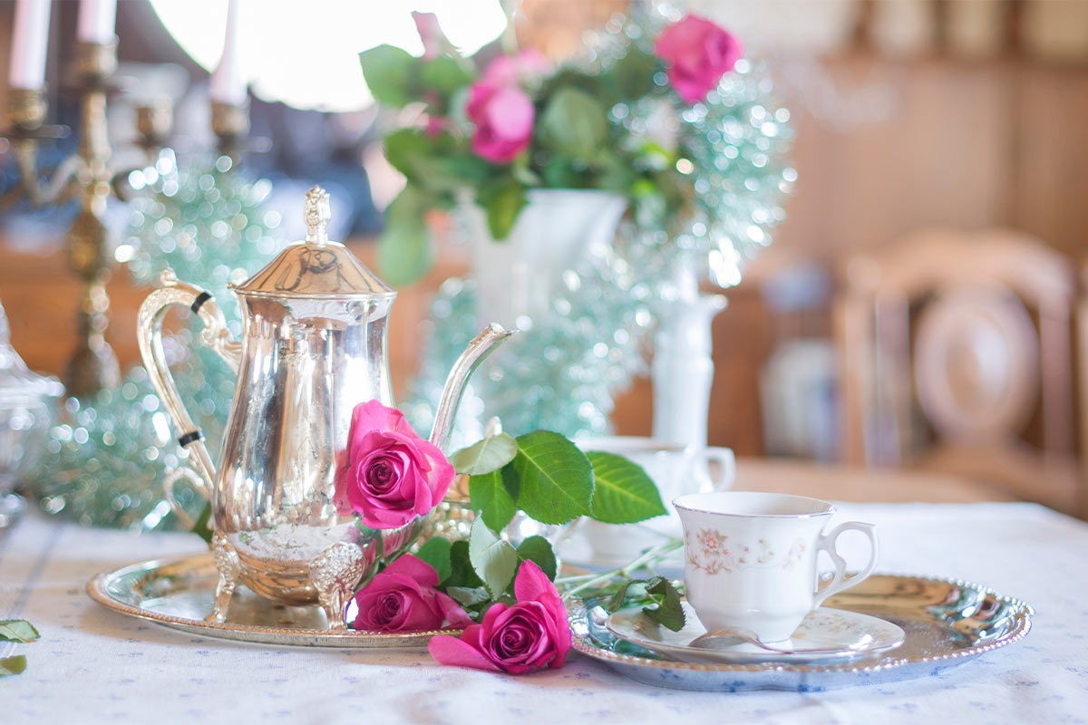 A close up photo of a tea kettle and a tea cup at a table with pink roses