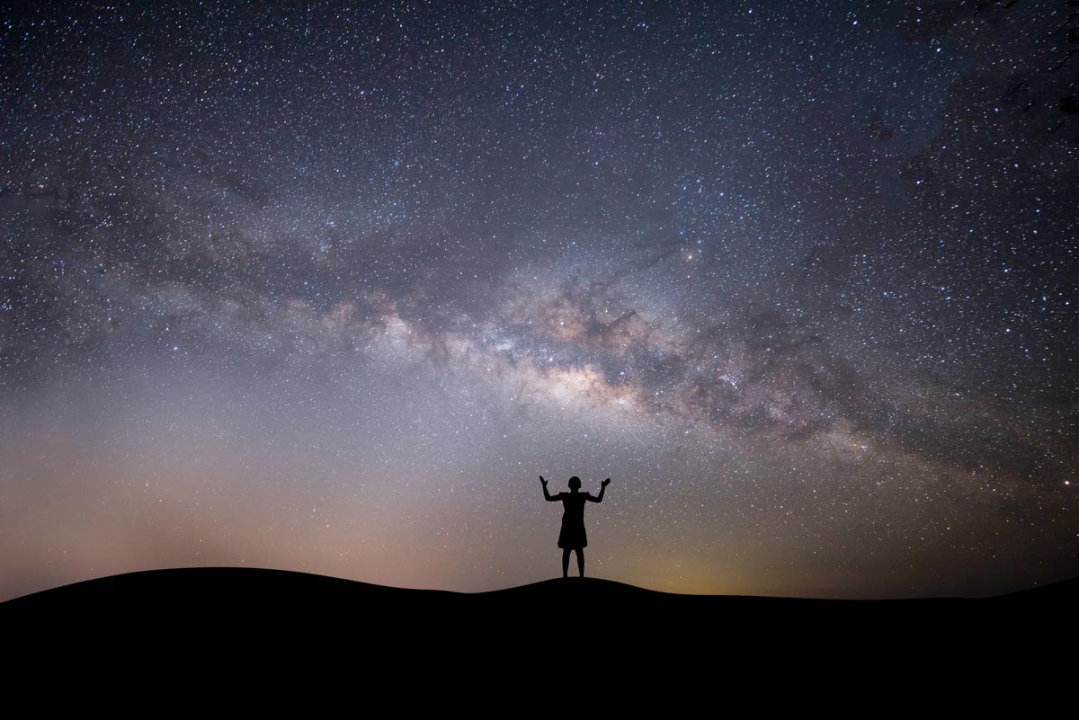 A shadow of a woman shrugging looking up at the sky and stars